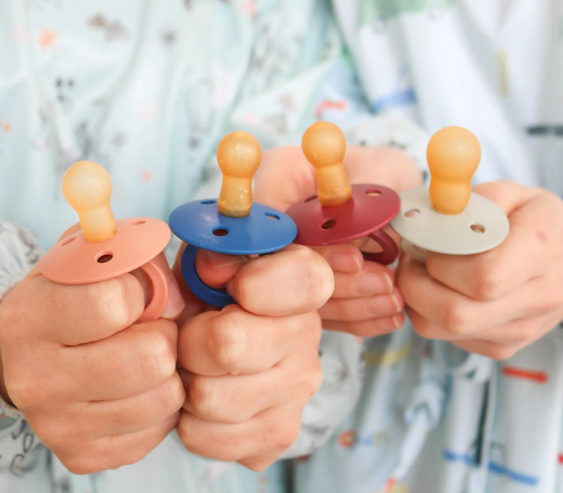 Mãos segurando chupetas coloridas no contexto do programa de remoção de chupeta na Clínica Júnior